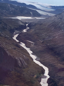 Aerial view of a pale glacial river winding through a dark rocky valley toward an ice sheet