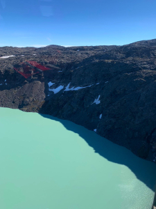 Aerial view of a turquoise glacial lake beside a dark rocky mountainside