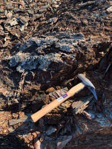 Geological hammer resting on a fractured mineralised outcrop